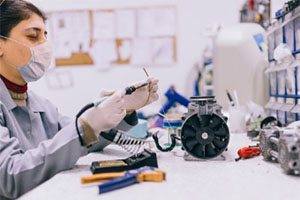 A woman in a lab coat operates a complex machine in a laboratory setting, focused on her task.